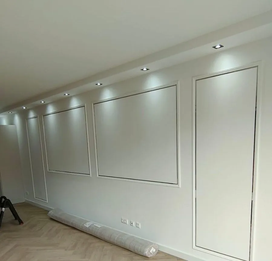 Woonkamerwand met strak afgewerkte wandlijsten en verlichting in een verlaagd plafond